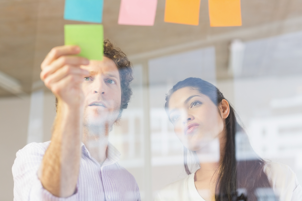 Businessman and businesswoman sticking adhesive notes on glass wall in office